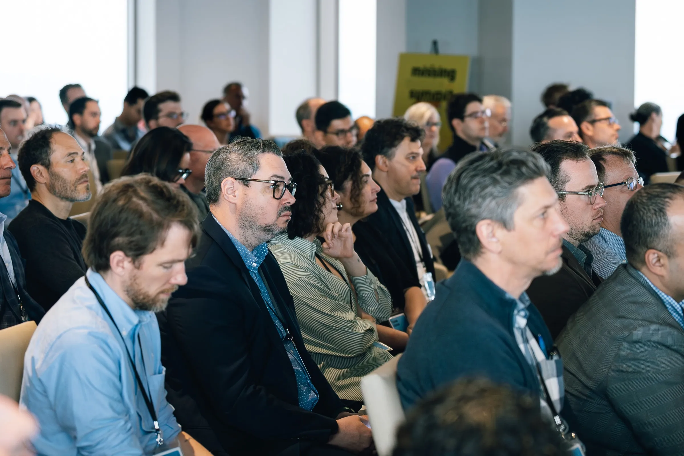 Attendees sit closely in rows, listening, a yellow Missing Middle Summit sign at the back of the room.