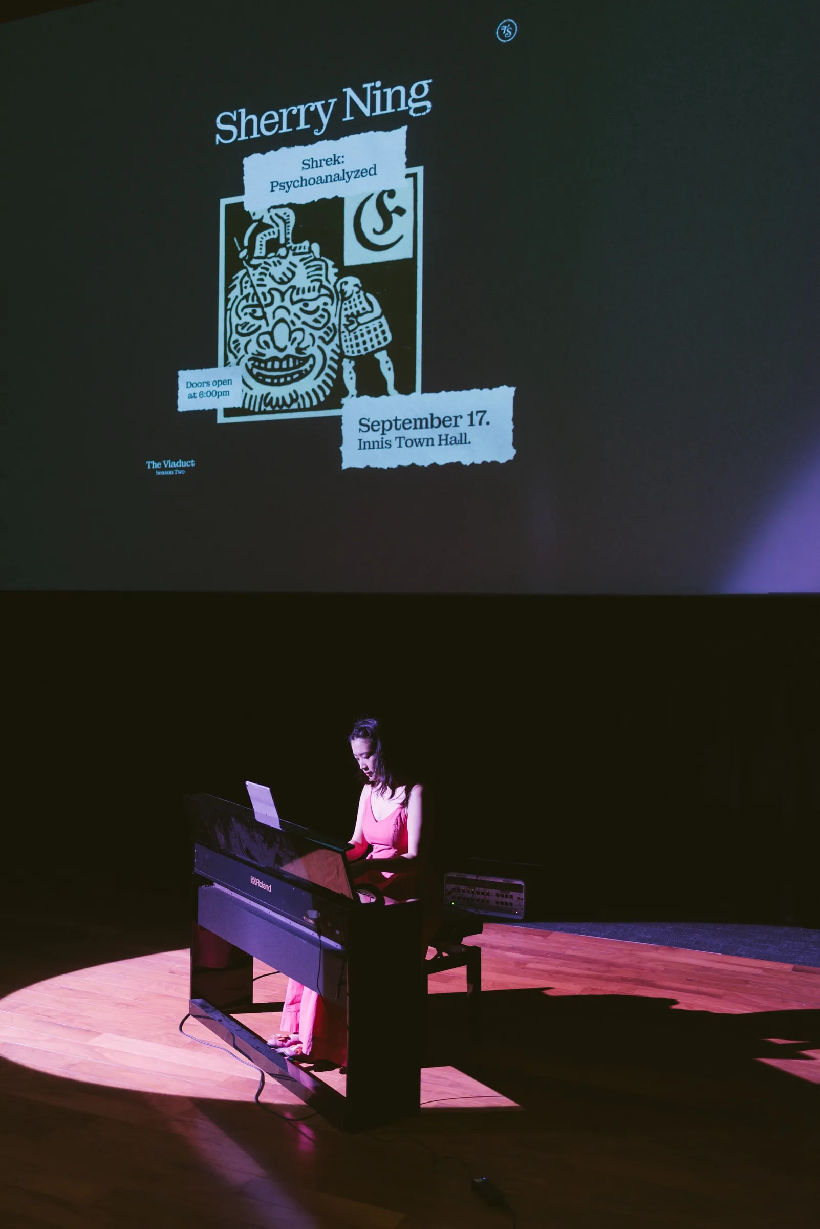 A musician plays a keyboard in a pool of stage light, the talk's title slide for the September 17 Innis Town Hall event projected on the screen above.