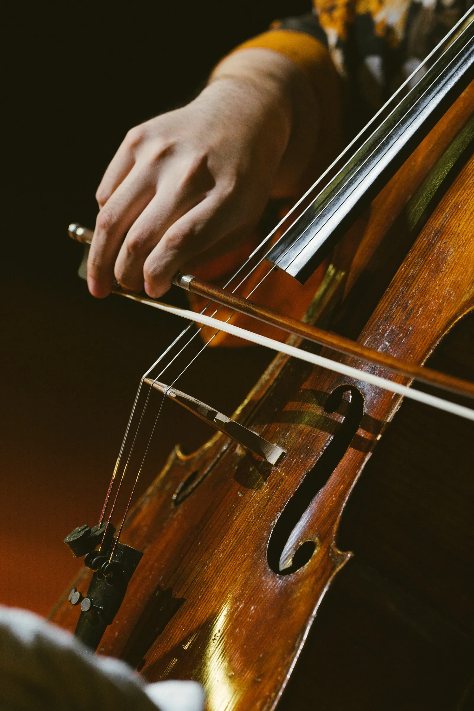 A close-up of a cellist's hand drawing the bow across the strings of a cello.