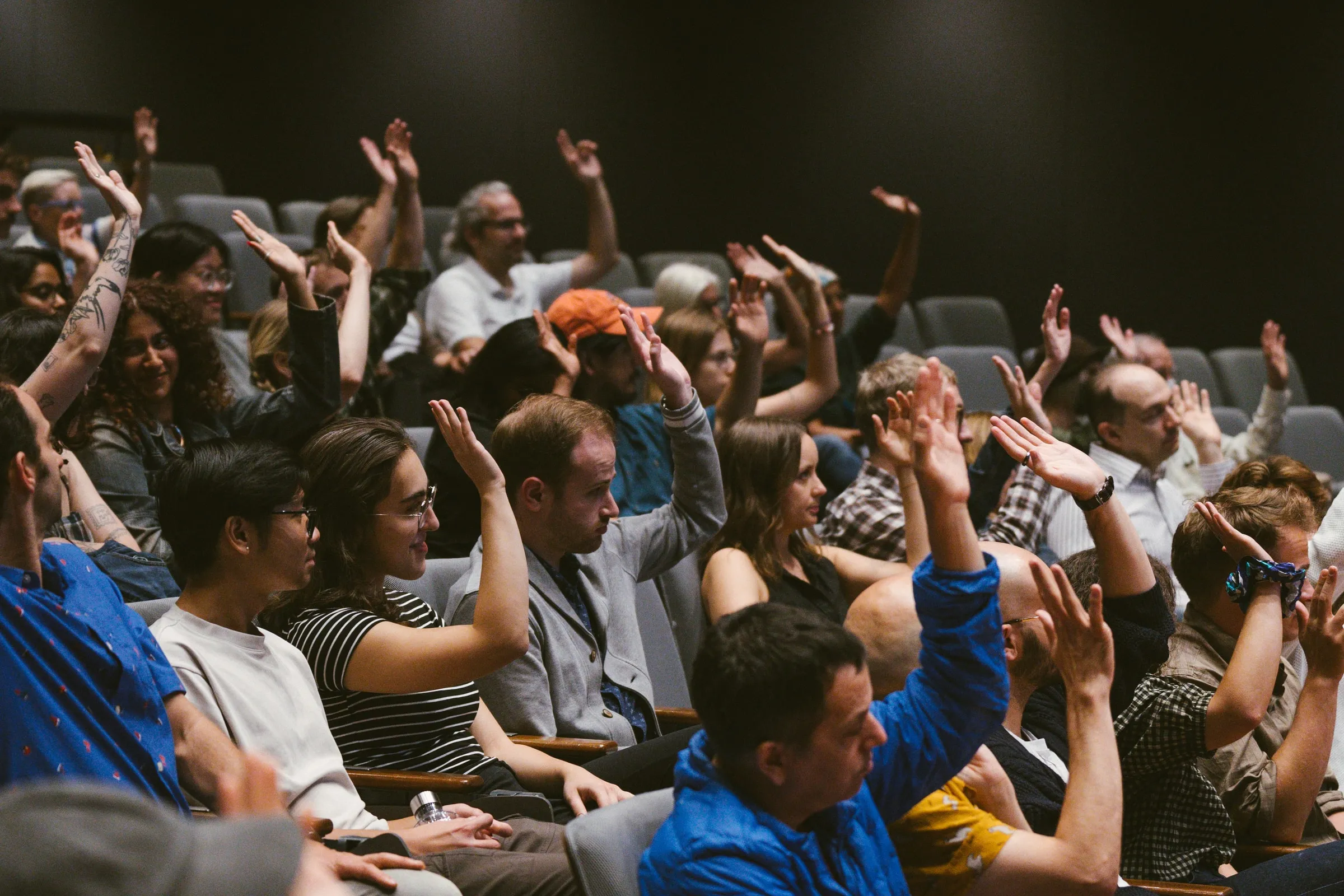 Audience members raise their hands in the theatre seats during the talk.